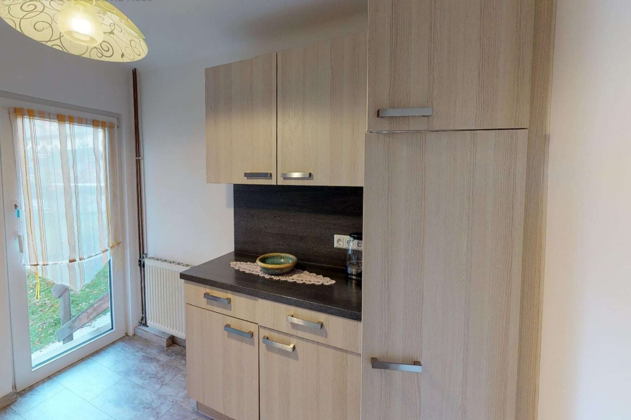 Une cuisine avec des meubles de rangement en bois, un plan de travail noir et un saladier posé sur le plan de travail.