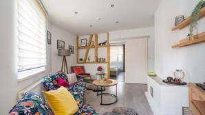 A living room with a sofa, a small round table, and a kitchen area with a counter and shelves. - Rückzugsort mit Waldblick (Zella-Mehlis)