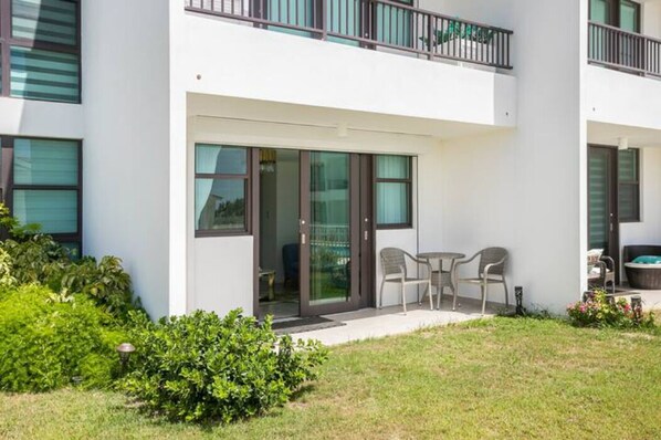 Un bâtiment moderne doté d’un balcon, de portes-fenêtres coulissantes et d’un petit espace patio aménagé avec des chaises.