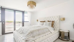 Een moderne slaapkamer met een groot bed, een kroonluchter en uitzicht door een schuifdeur.