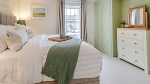 Une chambre bien rangée, avec un lit, une commode, une fenêtre avec des rideaux et un tableau accroché au mur.