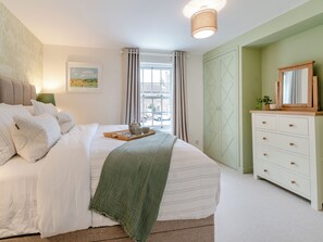 Un dormitorio ordenado con cama, cómoda, ventana con cortinas y un cuadro en la pared.