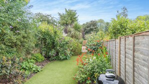 Un jardin avec une clôture en bois, un barbecue et une variété de plantes et de fleurs.