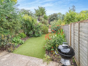 A garden with a wooden fence, a barbecue grill, and a variety of plants and flowers.