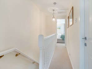 A hallway with a white railing, a light fixture, and a door leading to a bedroom.