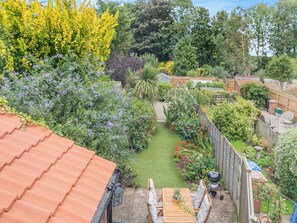 A garden with a patio, a barbecue, and a variety of plants and trees.