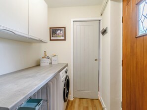 A laundry area with a washing machine, drying rack, and storage bins labeled 'Washing' and 'Pigs.'