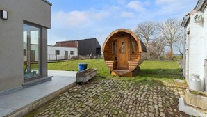 A modern building with a large wooden barrel-shaped structure in the yard. - Charming Cottage with Sauna (Honnelles)