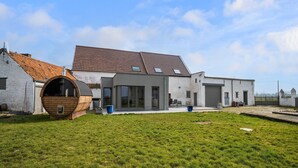 A modern house with a large barrel-shaped structure in the front, a garage, and a well-maintained lawn. - Charming Cottage with Sauna (Honnelles)