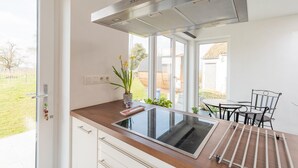 A modern kitchen with a built-in stove, a stainless steel range hood, and a view of the garden through large windows. - Charming Cottage with Sauna (Honnelles)