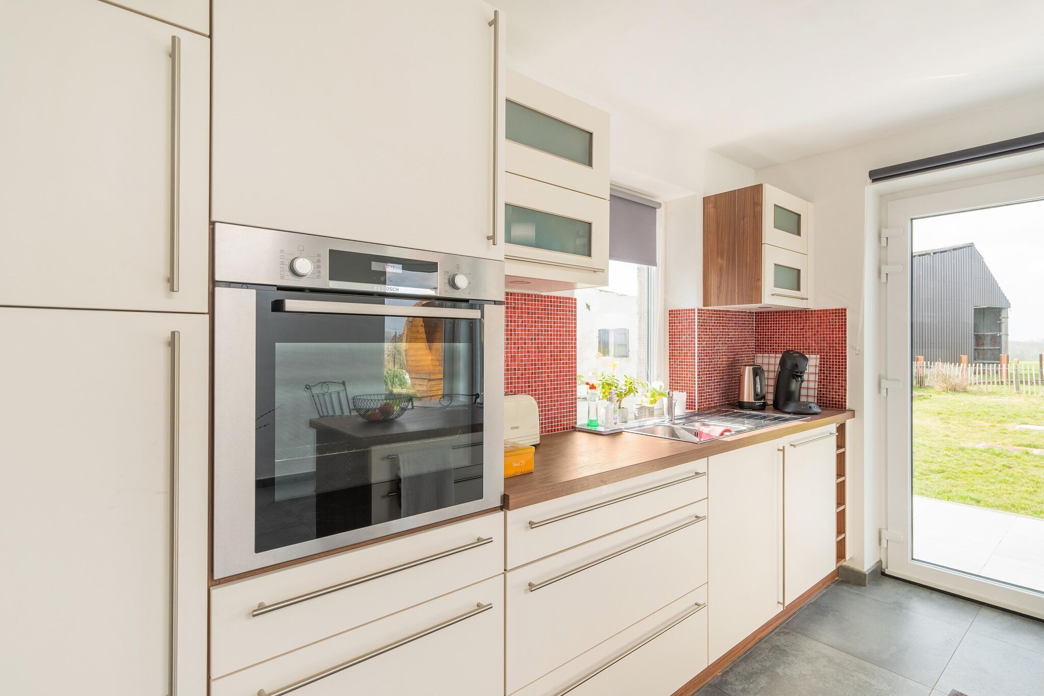 A modern kitchen with white cabinetry, a built-in oven, and a red-tiled backsplash.