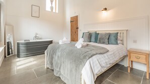 A bedroom with a bed, bedside table, and a bathroom with a bathtub. - The Red Rooster - UK44440 (Arlingham, near Frampton-on-Severn)