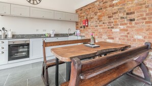 A kitchen with white cabinets, a brick wall, a wooden bench, and a clock. - The Red Rooster - UK44440 (Arlingham, near Frampton-on-Severn)