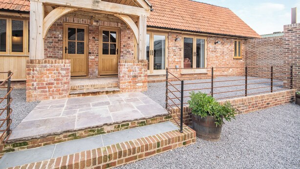 A brick building with a tiled roof, wooden doors, and a gravel driveway. - The Red Rooster - UK44440 (Arlingham, near Frampton-on-Severn)