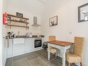 A compact kitchen with white cabinets, a built-in oven, a sink, and a dining area with a wooden table and wicker chairs.