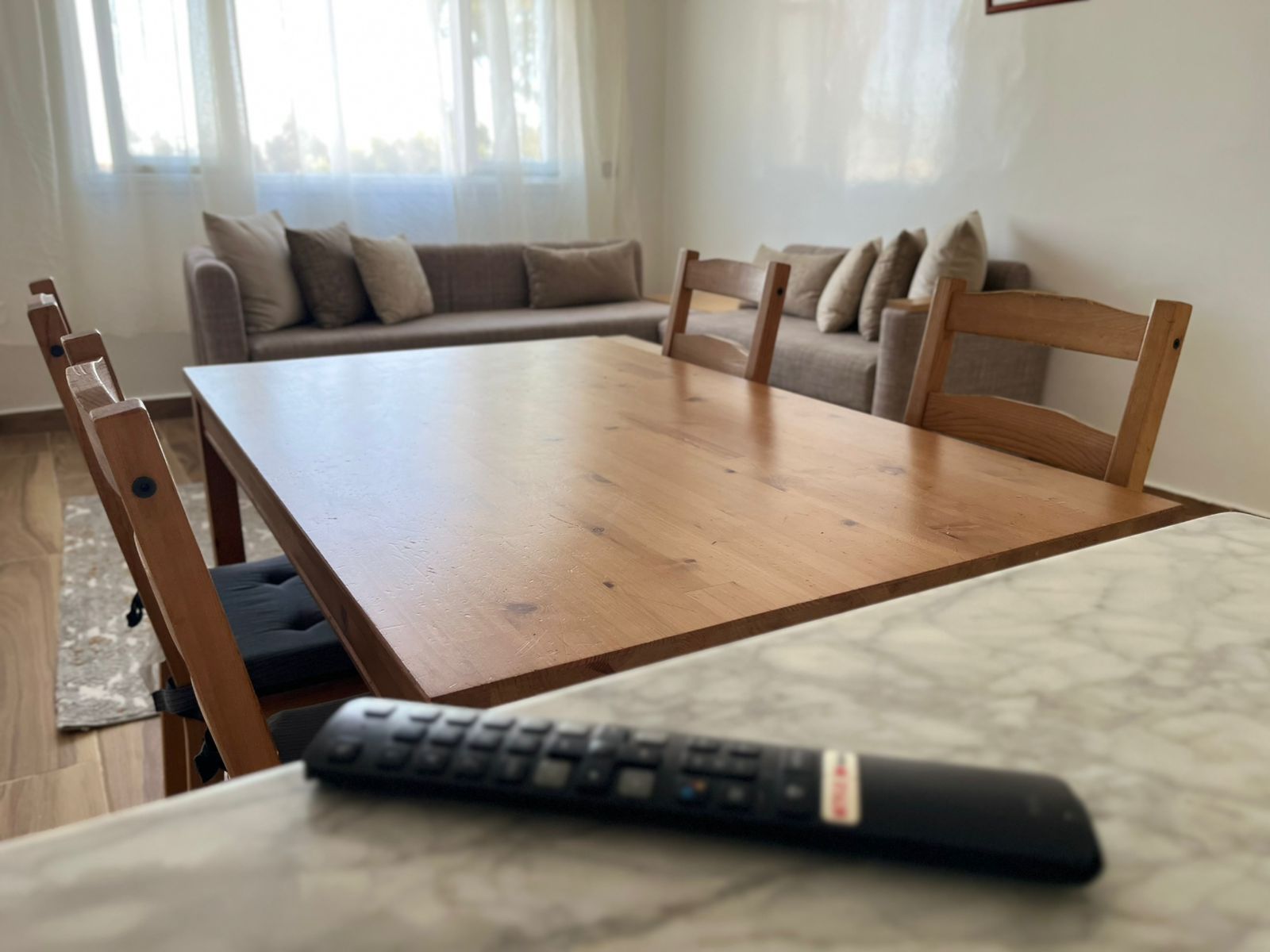 Ein Esstisch mit Stühlen, eine Fernbedienung auf dem Tisch und eine Couch im Hintergrund.