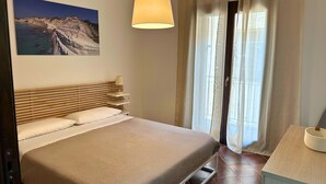 Un dormitorio con cama, lámpara de noche y un cuadro de un paisaje costero.