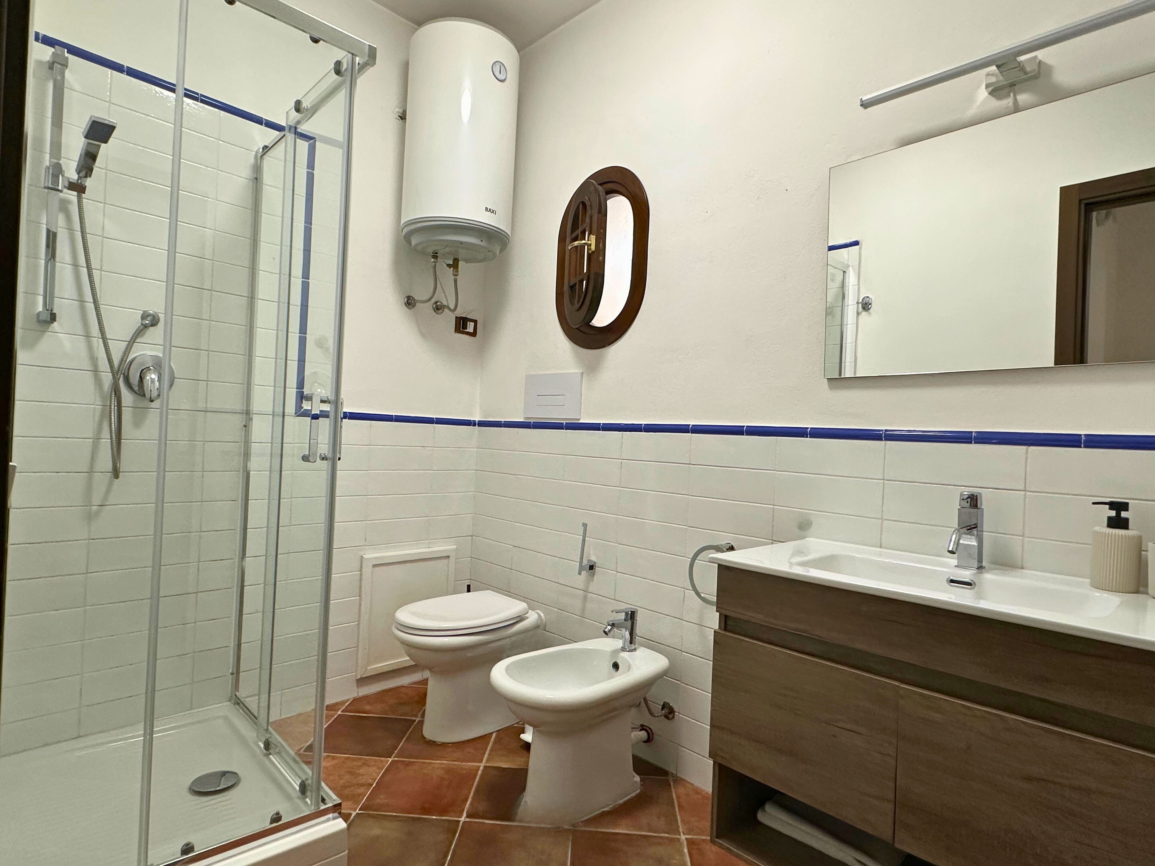 Un bagno con box doccia in vetro, due servizi igienici, un bidet, un lavandino con specchio e un porta asciugamani.