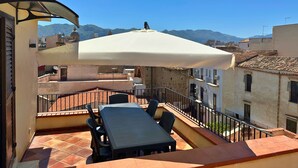 Una terraza con mesa y sillas, un paraguas y vistas a edificios y montañas.
