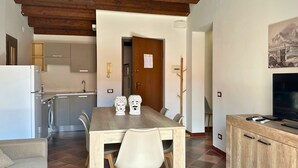 Una cocina moderna con techo de madera, un comedor con mesa y sillas de madera, un sofá y un televisor sobre un mueble de madera.