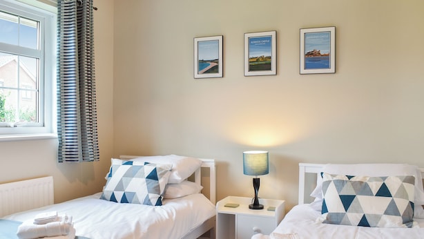 Une chambre double avec deux lits, une table de chevet avec une lampe, une fenêtre avec des rideaux et trois tableaux encadrés accrochés au mur.