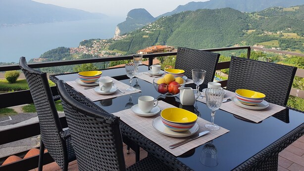 A table set with plates, bowls, and glasses, overlooking a mountainous landscape with a view of the sea. - Casa Irene le Balze apartment lake view (Tremosine)