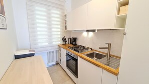 A compact kitchen with a gas stove, oven, and sink, wooden countertop, and white cabinetry.