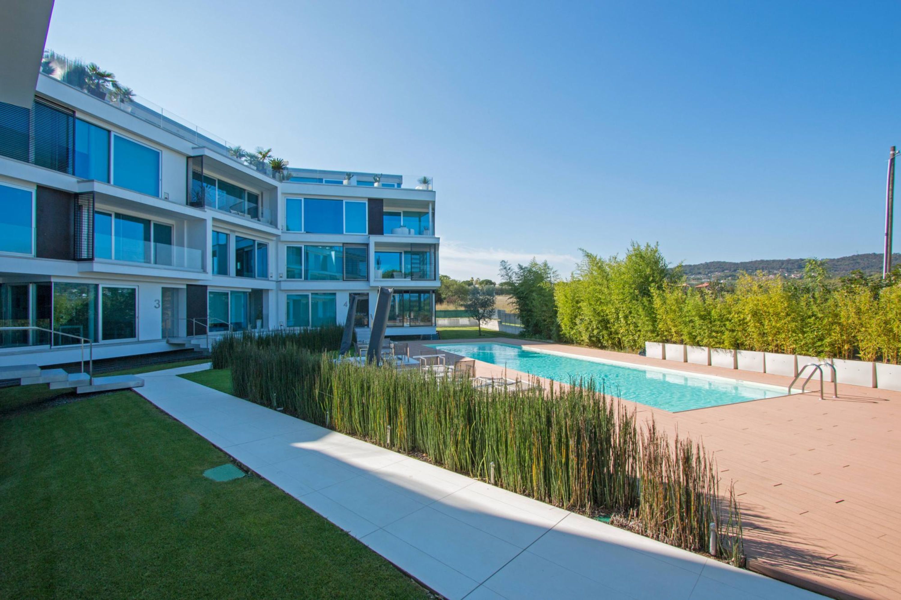 A modern multi-story building with a swimming pool, surrounded by well-maintained grass and plants.