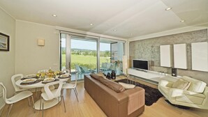 A modern living room with a dining area, a sofa, a TV, and a large window offering a view of the outdoors. - Bristol Exclusive 2 5 by Wonderful Italy (Lonato del Garda)