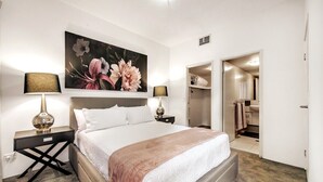 Et pænt indrettet hotelværelse med en stor seng, to sengeborde med lamper, et stort blomsterbillede på væggen og et walk-in closet.