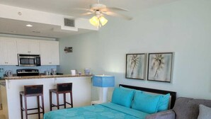 A bedroom with a bed, a sofa, a coffee table, a desk, a chair, a ceiling fan, and a kitchenette.