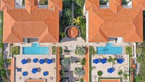 An aerial view of a resort with two swimming pools, lounge areas, and a central circular garden.