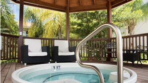 A hot tub with a wooden deck, two white cushioned chairs, and a metal ladder.