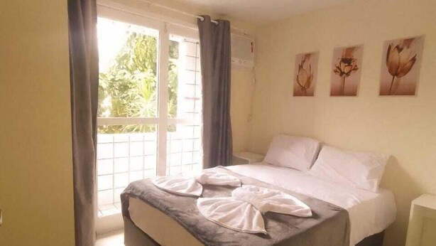 A bedroom with a bed, a nightstand, a window with curtains, and wall art. - Residencial Terrazas (Florianópolis)