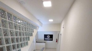 A clean, modern hallway with a glass wall on one side, a sign for 'TERRAZAS DEL REPARTO', and a fire extinguisher on the wall. - Residencial Terrazas (Florianópolis)