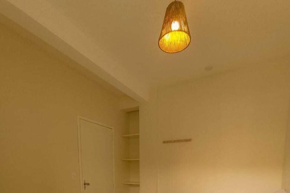 A hotel room with two beds, a wardrobe, a shelf, and a hanging light fixture.