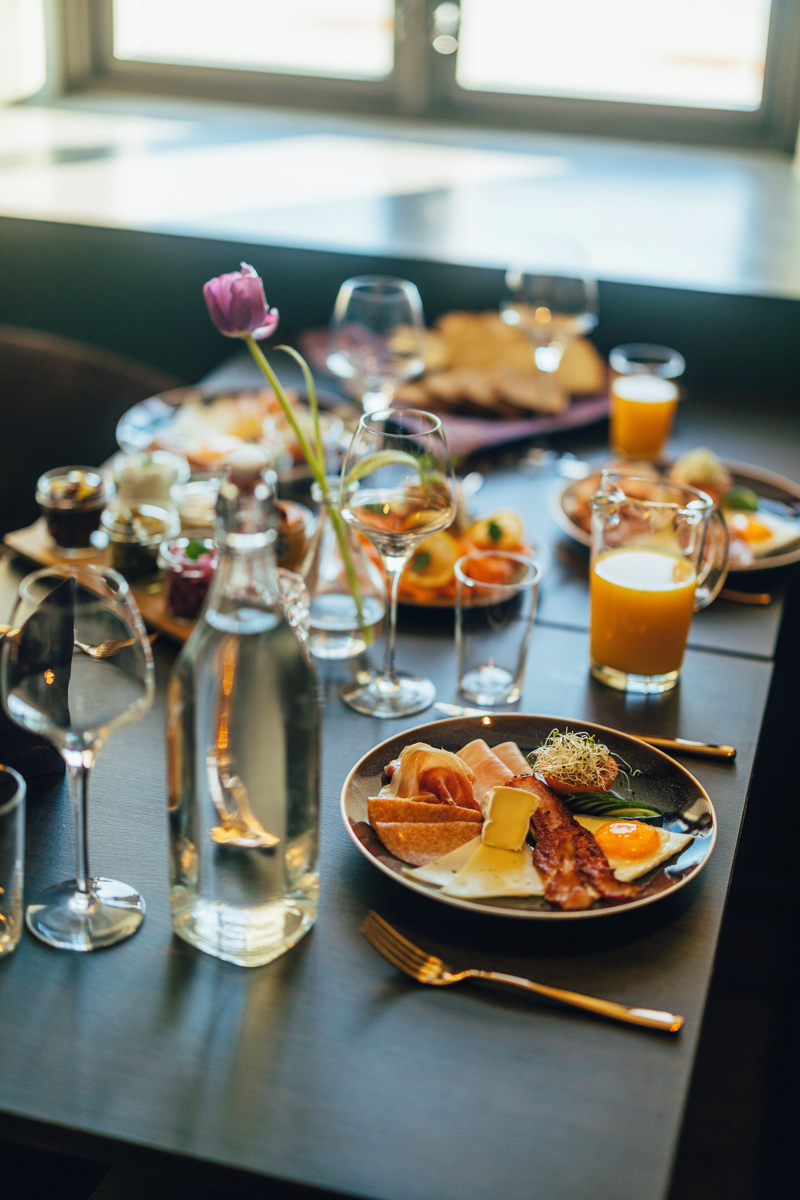 A breakfast setting with a variety of dishes, glasses, and a bottle on a table.