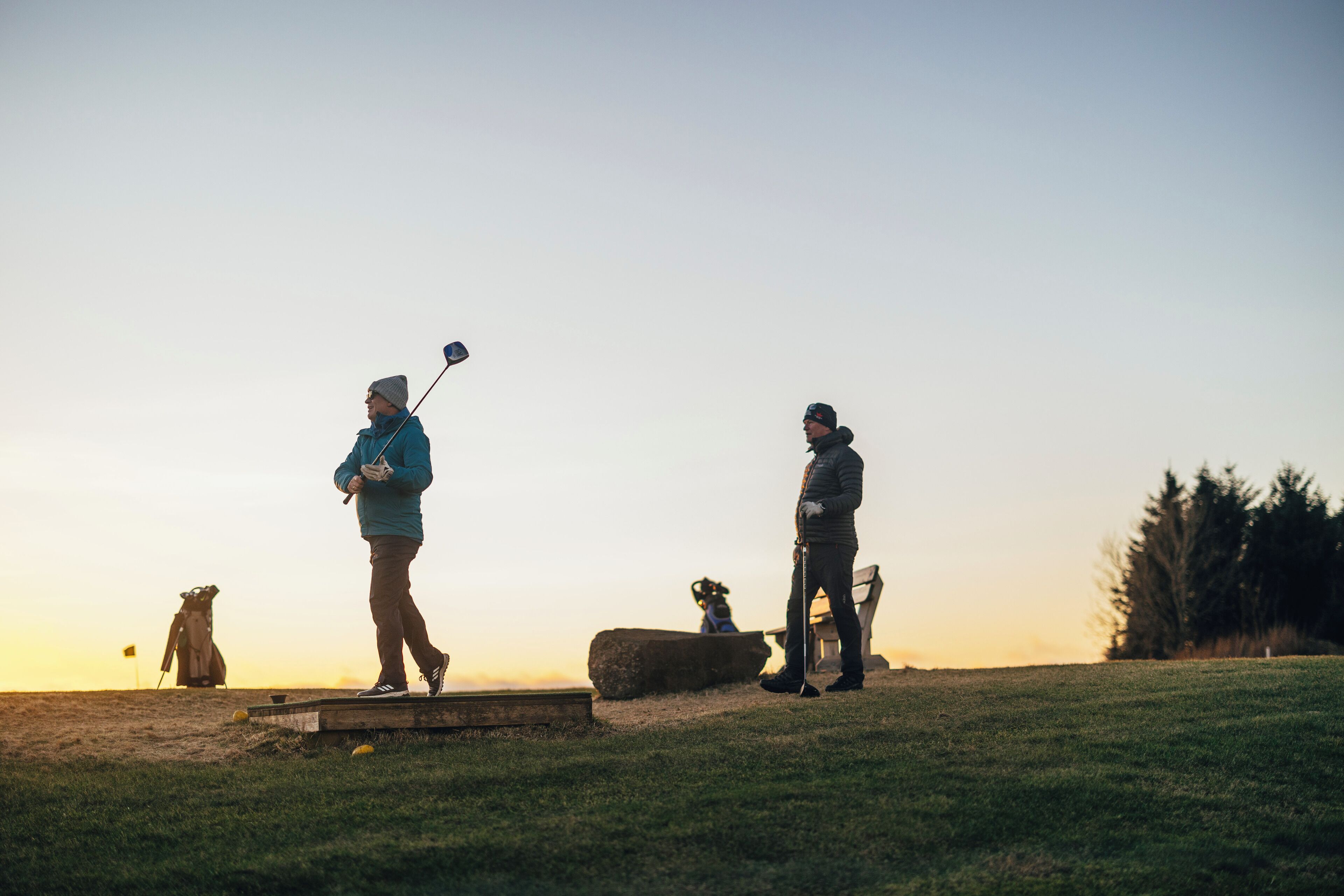 A golf course at sunset with players and equipment.