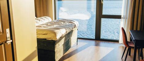 A bedroom with a bed, a view of a body of water, and a dining area with a table and chairs.