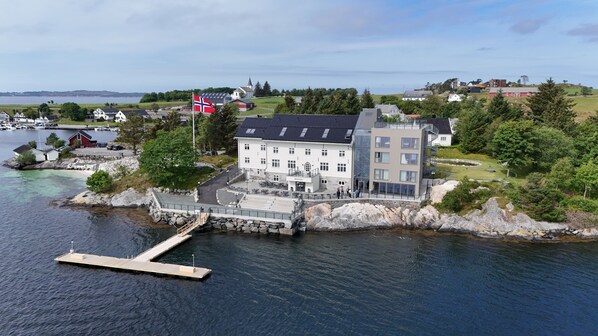 Un edificio costero con un muelle, rodeado de vegetación y una bandera.