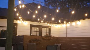Un espace extérieur aménagé en terrasse, avec des guirlandes lumineuses, des bancs en bois et une table.