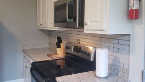 Une cuisine avec des armoires blanches, un four à micro-ondes en acier inoxydable, une cuisinière et un extincteur fixé au mur.