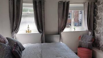 Ein Schlafzimmer mit einem Bett, zwei Vorhängen, einem Heizkörper und einem kleinen Tisch mit einer Flasche und Kerzen.