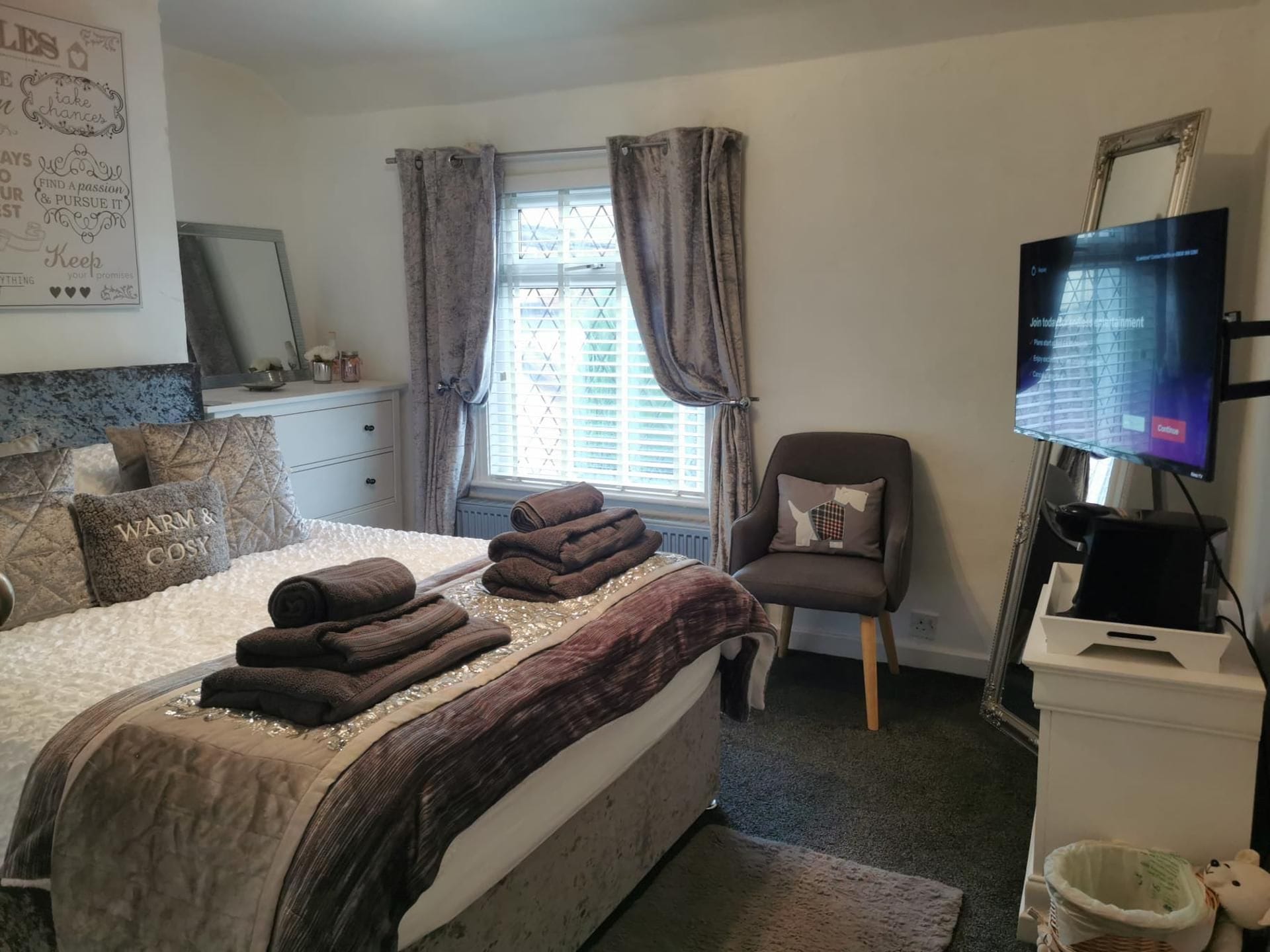 A bedroom with a bed, a chair, a television, and a window with curtains.