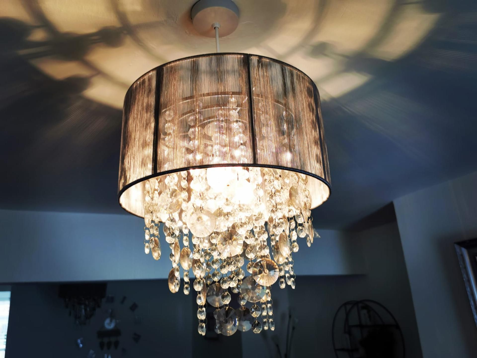 En ljuskrona med en cylindrisk lampskärm och kristallprydnader.