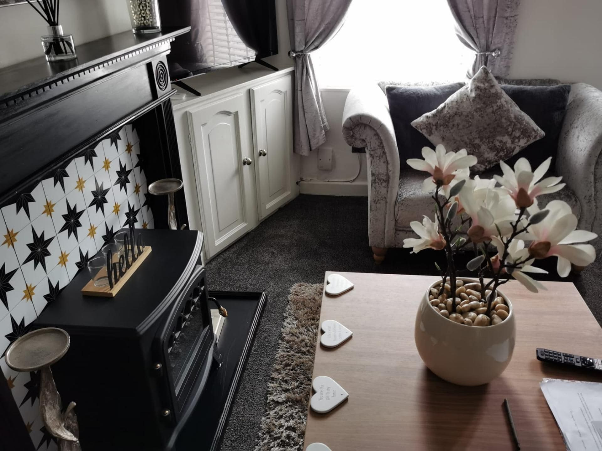 Een woonkamer met een zwart-wit betegelde muur, een bank, een bijzettafeltje met bloemen en een open haard.