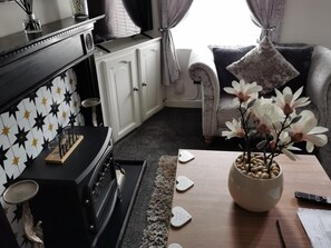 A living room with a black and white tiled wall, a sofa, a coffee table with a flower arrangement, and a fireplace. - 2-bed House in Macclesfield Cheshire (Macclesfield)