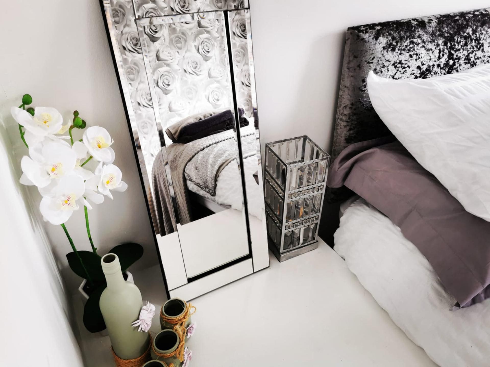 A bedroom with a bed, a mirror, and a vase with flowers.