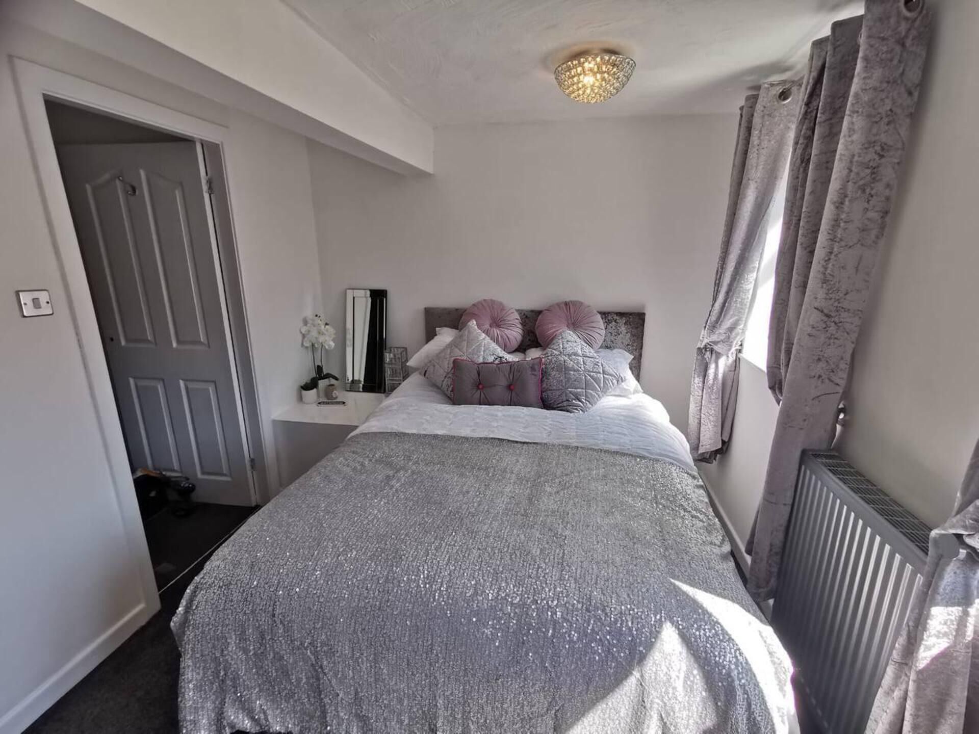 A bedroom with a bed, a bedside table, a mirror, and a radiator.