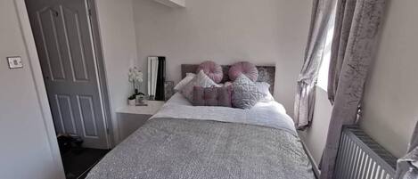 A bedroom with a bed, a bedside table, a mirror, and a radiator.